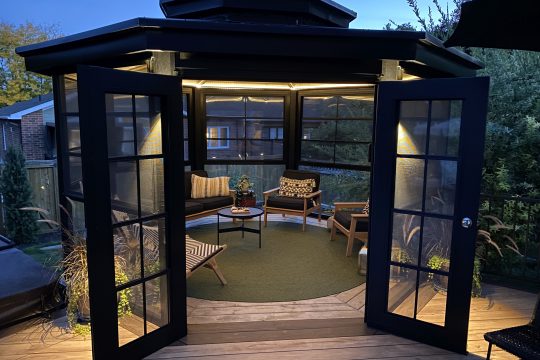 Cosy enclosed gazebo at dusk with black 4-track windows and open French doors