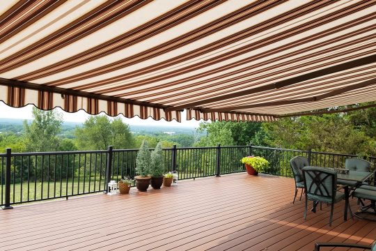 Brown and cream striped retractable awning shading a wide hilltop deck with patio furniture