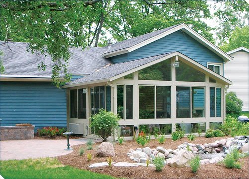 Betterliving gable-roof sunroom addition on a blue-sided home with landscaped garden