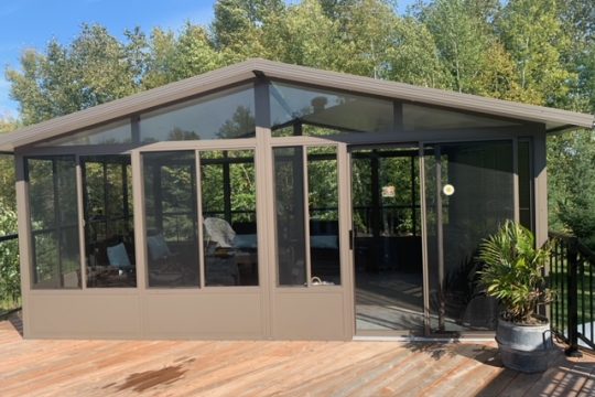 Taupe freestanding aluminum gazebo with gable roof on a wood deck surrounded by trees