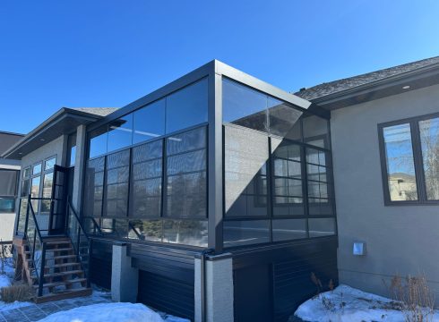 Dark-framed Grand Vista sunroom with glass gable on a stucco home in winter